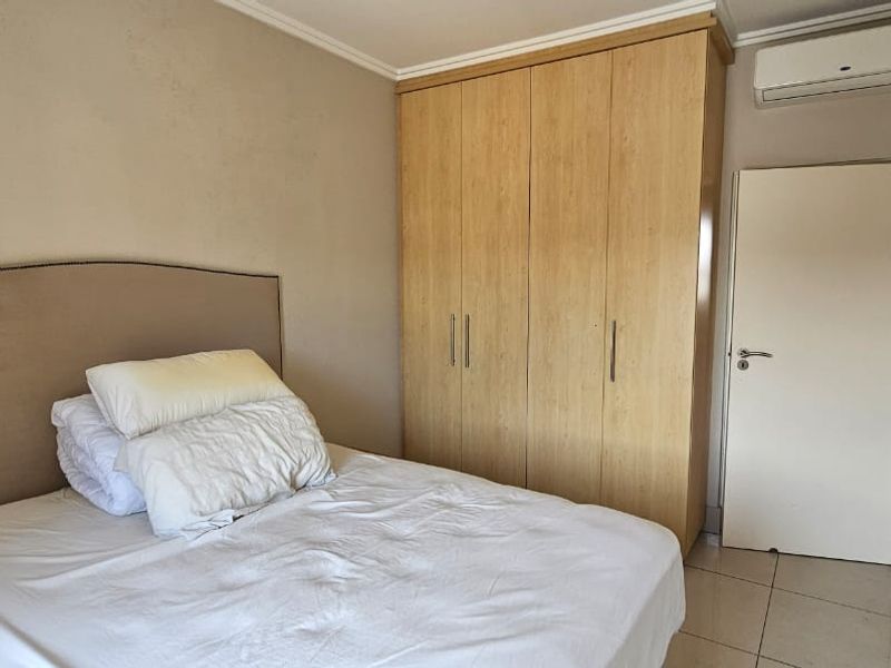 A well-maintained bedroom featuring built-in wooden wardrobes, tiled flooring, and a wall-mounted split-system air conditioning unit.