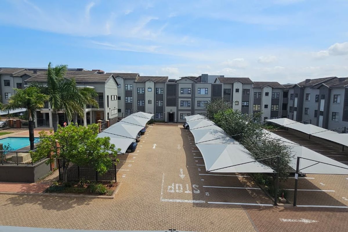 Aerial view of the apartment complex featuring a paved parking area with shade cloth carports and a communal swimming pool.