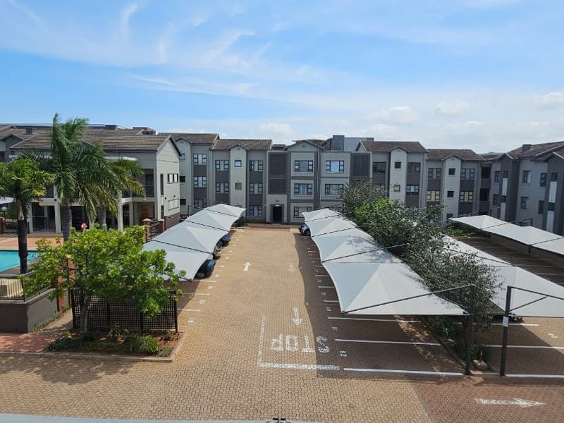 Aerial view of the apartment complex featuring a paved parking area with shade cloth carports and a communal swimming pool.