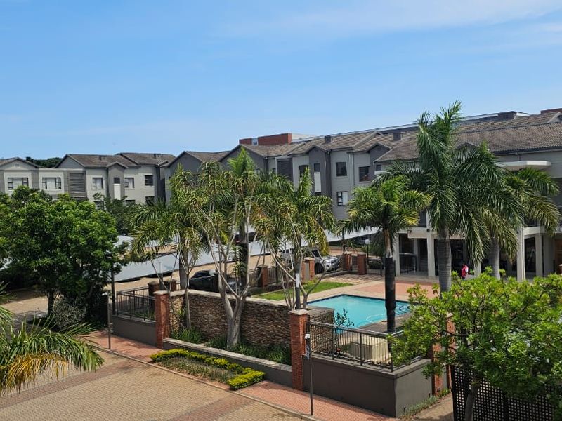 An elevated view of the apartment complex grounds, featuring a swimming pool, paved parking areas with shade structures, and established landscaping.