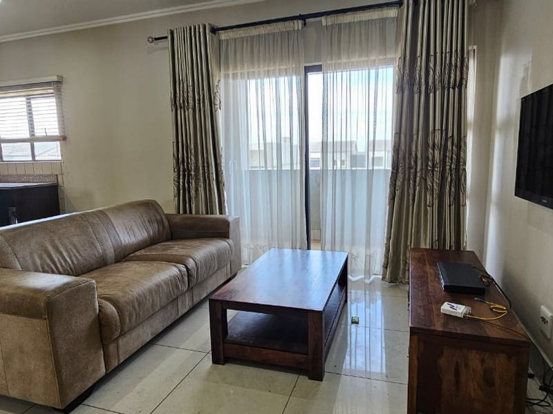 Open-plan living area featuring tiled floors, integrated kitchen cabinetry, and a sliding glass door providing access to the balcony.