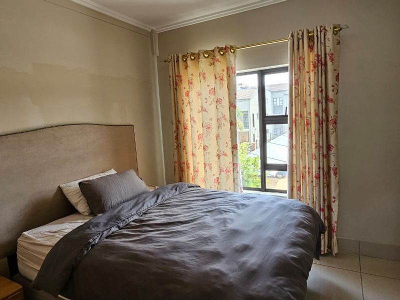 A bedroom featuring tiled flooring and a window, currently showing signs of wall paint wear and surface imperfections.