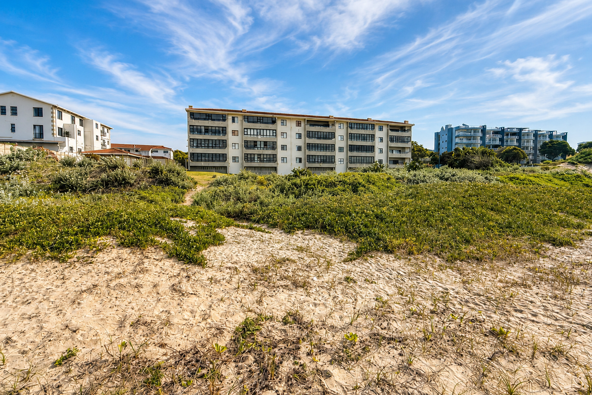 A view of the rear elevation of a multi-story apartment complex situated behind coastal sand dunes and natural vegetation.