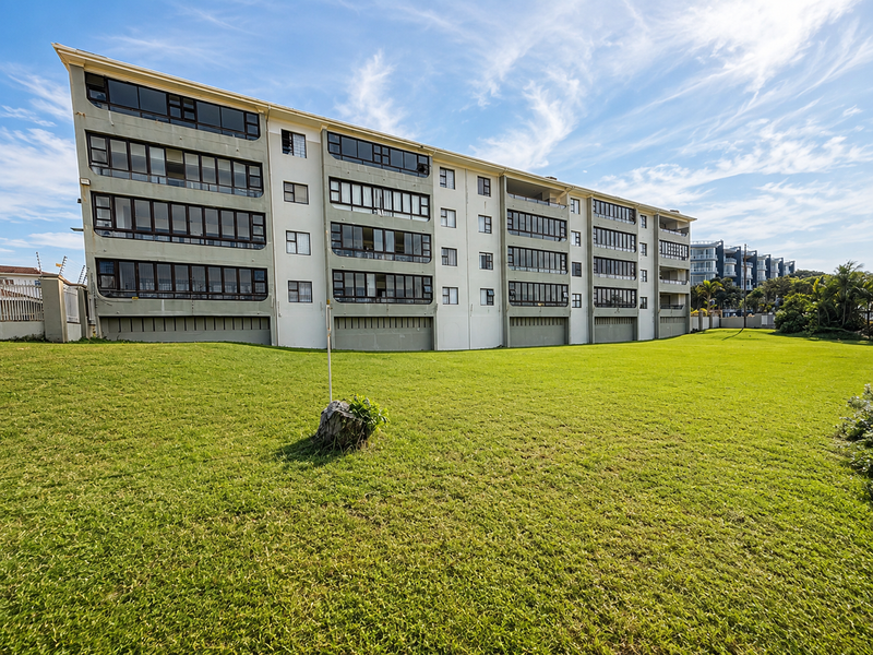 Rear view of a multi-story apartment complex featuring enclosed balconies and a well-maintained communal lawn area.