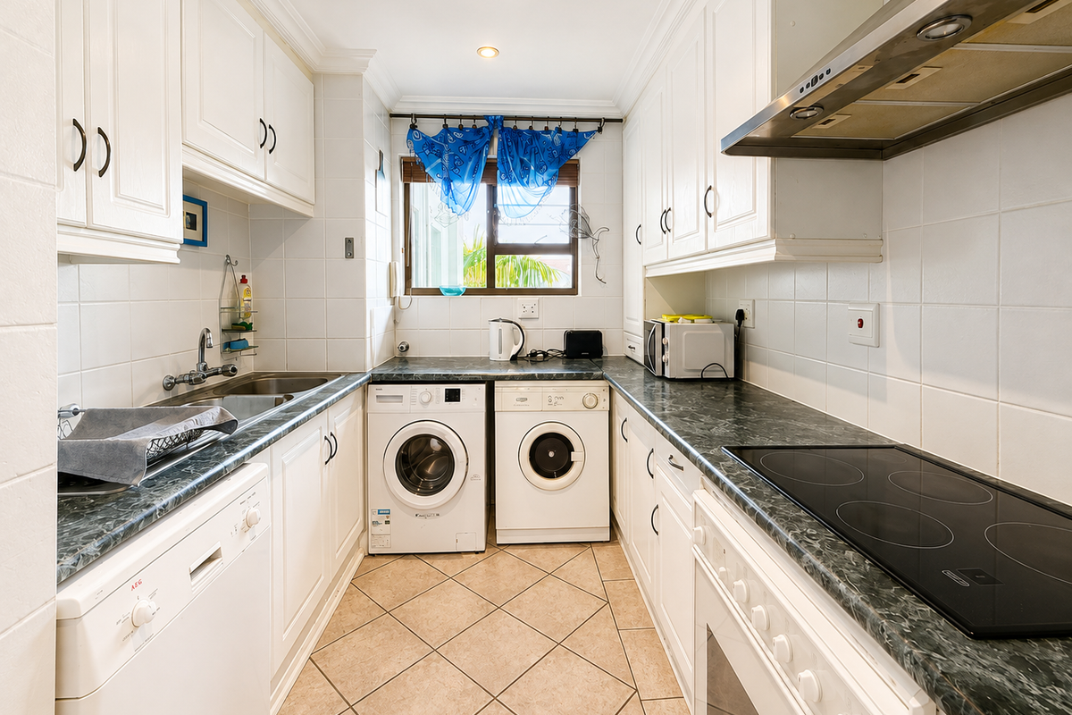 Functional galley-style kitchen featuring white cabinetry, dark laminate countertops, integrated appliances, tiled backsplash, and floor tiles.