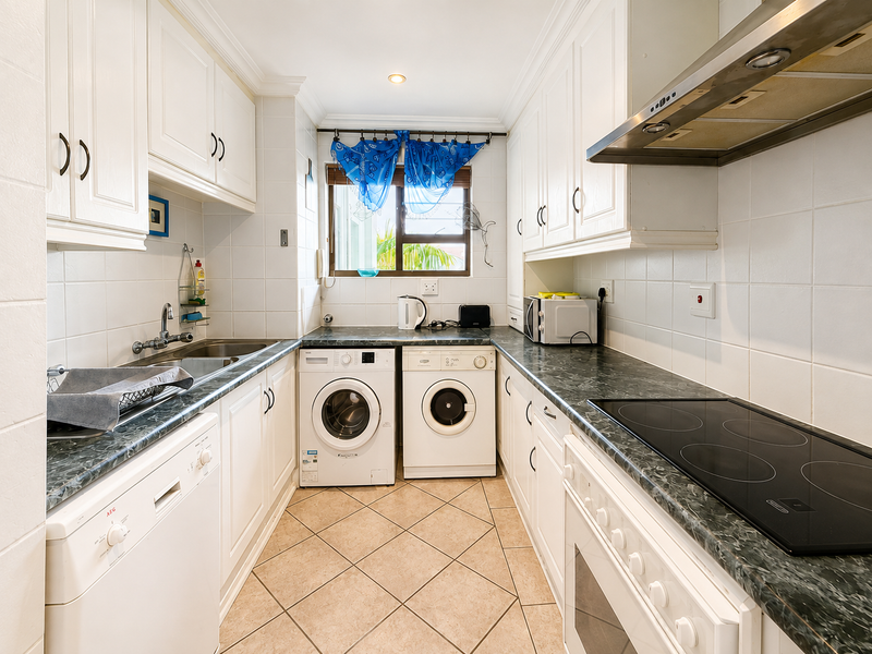 Functional galley-style kitchen featuring white cabinetry, dark laminate countertops, integrated appliances, tiled backsplash, and floor tiles.