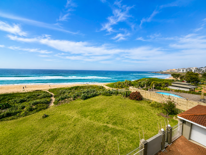 Elevated coastal view overlooking a private garden, swimming pool, and the beach, showcasing the property's prime seaside location.