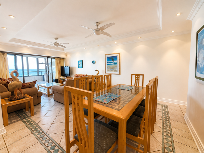 Spacious open-plan living and dining area featuring tiled floors with decorative borders, recessed lighting, ceiling fans, and direct access to a balcony with ocean views.