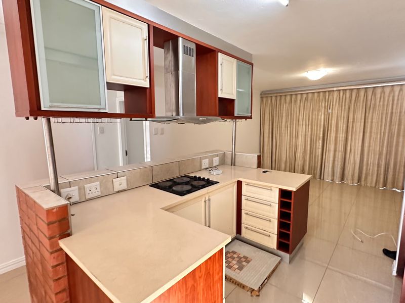 Open plan kitchen featuring built-in cabinetry, electric hob, and extractor fan, flowing into a spacious living area with tiled flooring.
