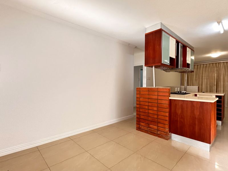 Open plan living and kitchen area featuring tiled floors, a brick feature wall, and built-in wooden cabinetry with a breakfast counter.
