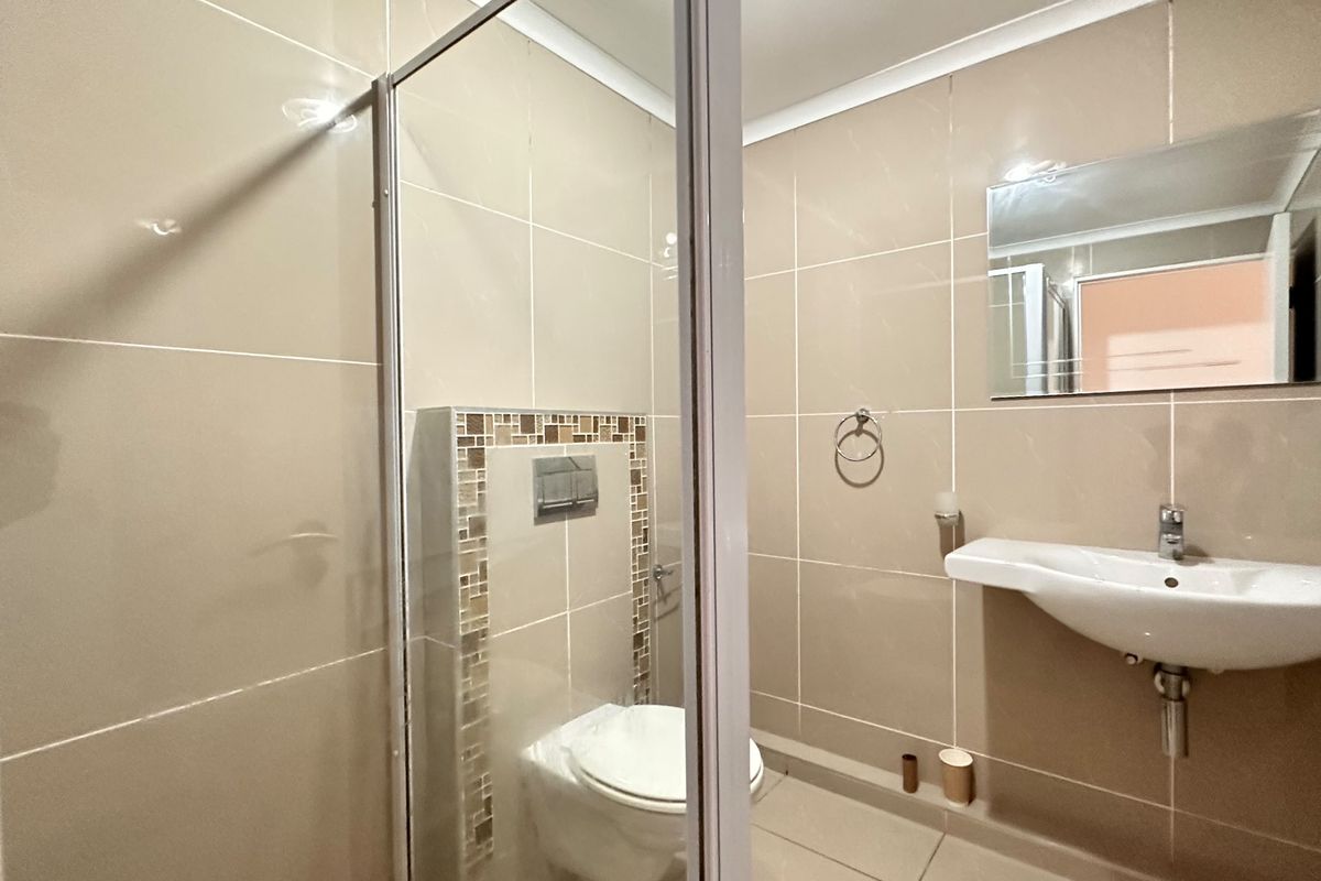 A clean, modern bathroom featuring a wall-mounted toilet with a concealed cistern, a glass shower enclosure, and a wall-mounted basin with a mirror.