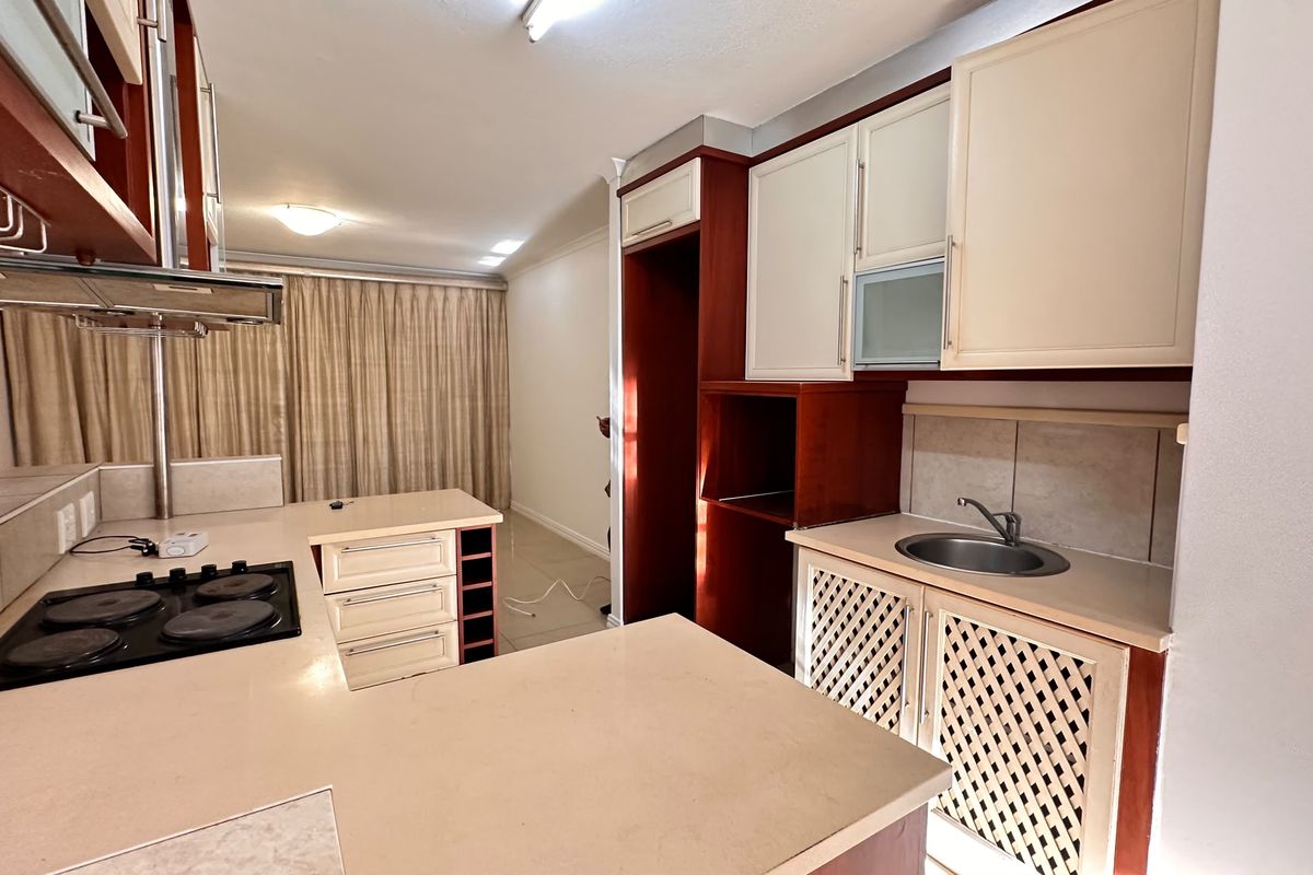 A functional kitchen featuring built-in cabinetry, an electric hob with extractor fan, and a stainless steel sink with tiled backsplash.