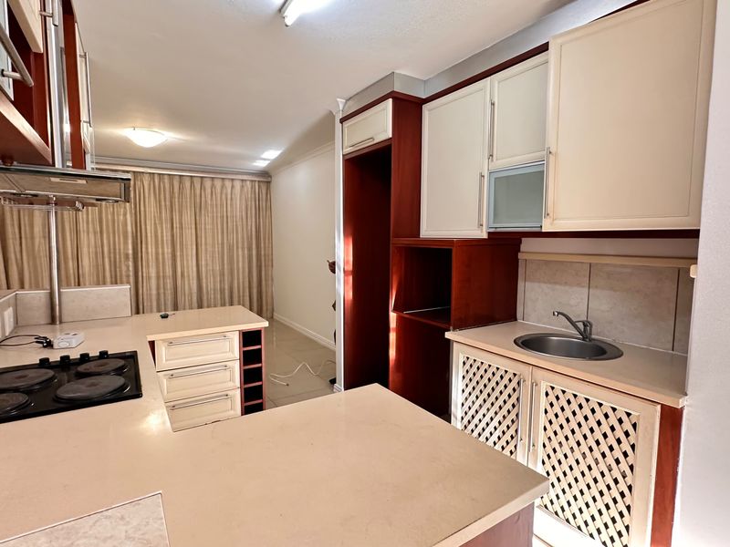 A functional kitchen featuring built-in cabinetry, an electric hob with extractor fan, and a stainless steel sink with tiled backsplash.