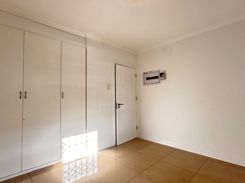 An empty bedroom featuring built-in cupboards, tiled flooring, and a wall-mounted electrical distribution board.