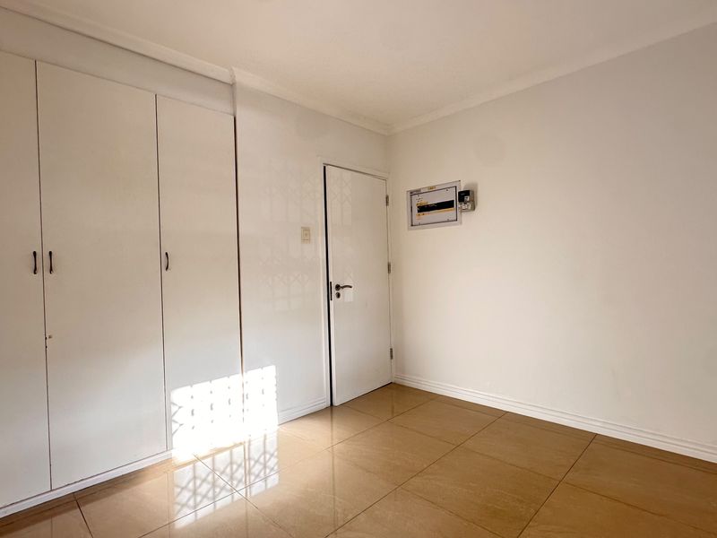 A clean, empty bedroom featuring neutral tiled flooring and ample built-in cupboard storage space.