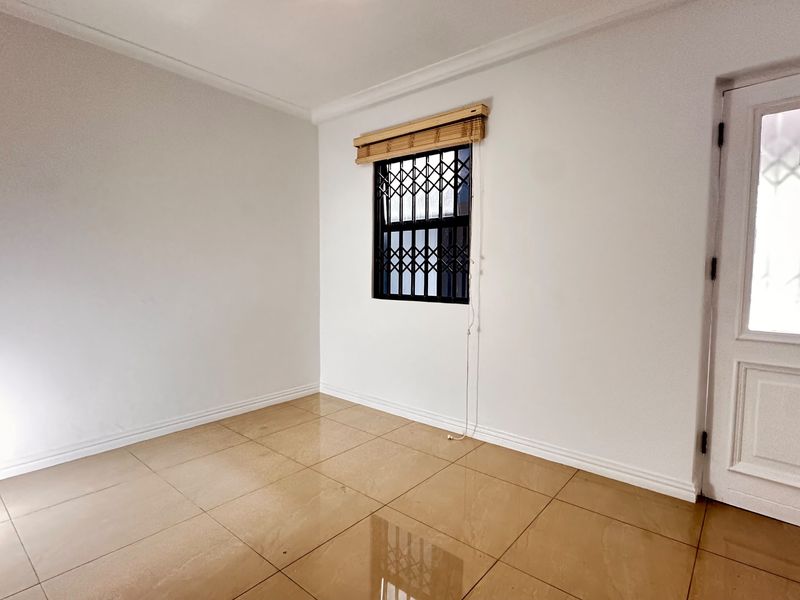 A clean, empty bedroom featuring neutral tiled flooring, white walls, and a window fitted with a security gate.