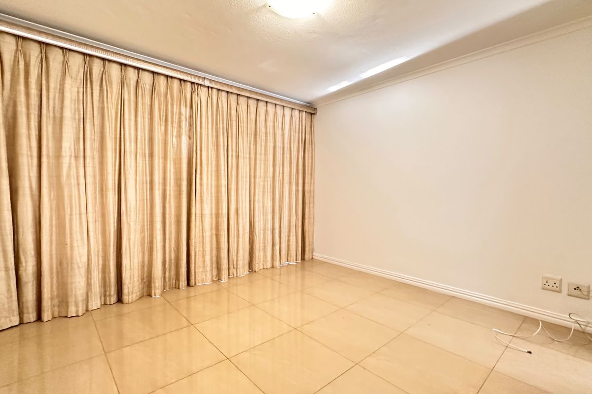 A bright, empty bedroom featuring neutral tiled flooring, a ceiling light fixture, and floor-to-ceiling curtain tracks.