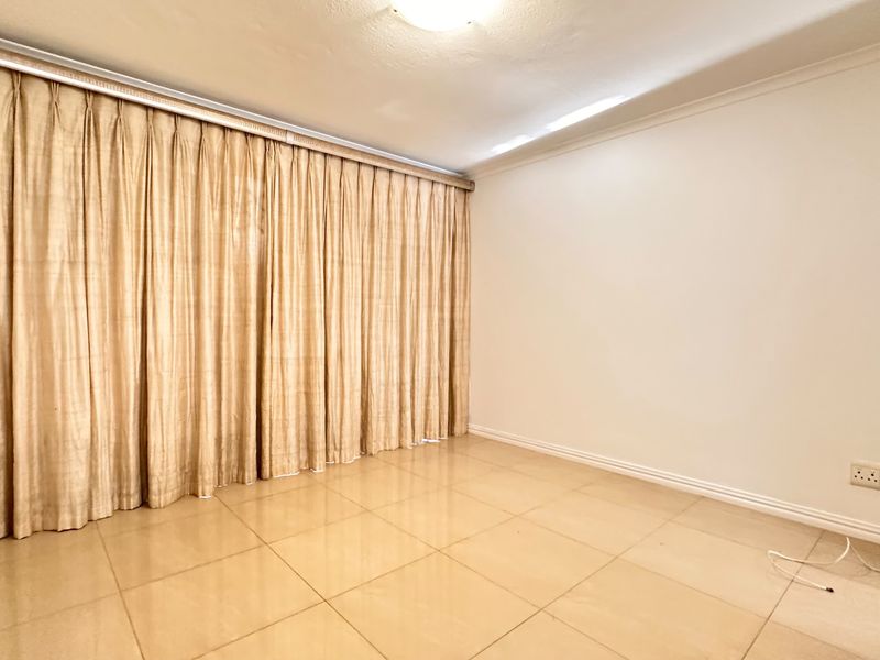 A bright, empty bedroom featuring neutral tiled flooring, a ceiling light fixture, and floor-to-ceiling curtain tracks.