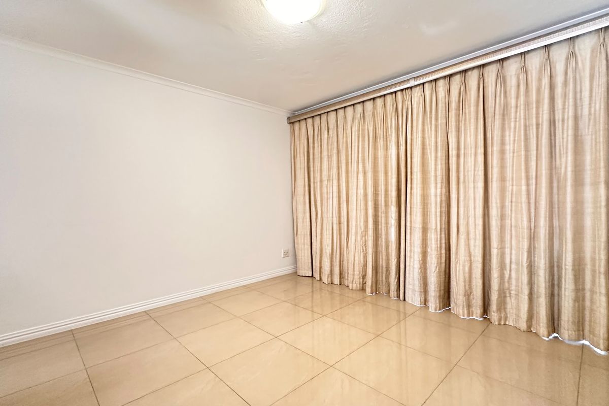 An empty living area featuring neutral tiled flooring and a full-length curtain track, providing a blank canvas for interior design.