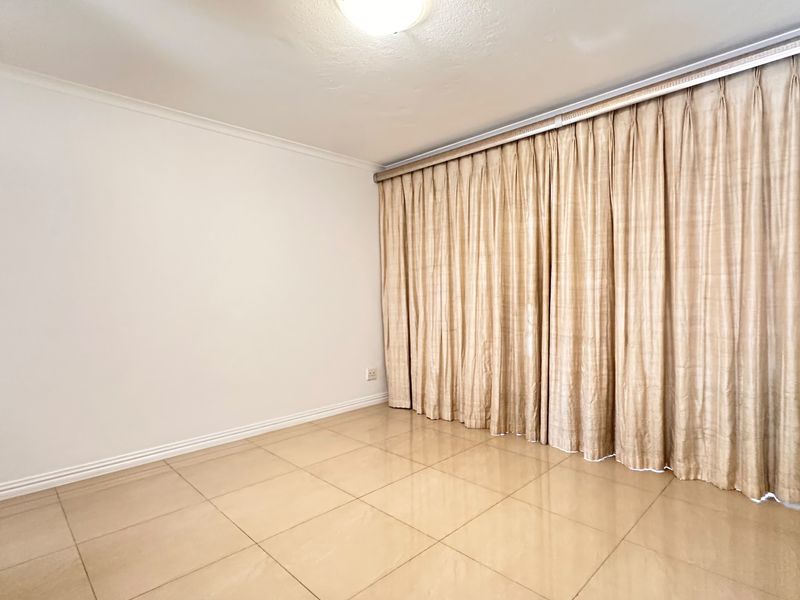 An empty living area featuring neutral tiled flooring and a full-length curtain track, providing a blank canvas for interior design.