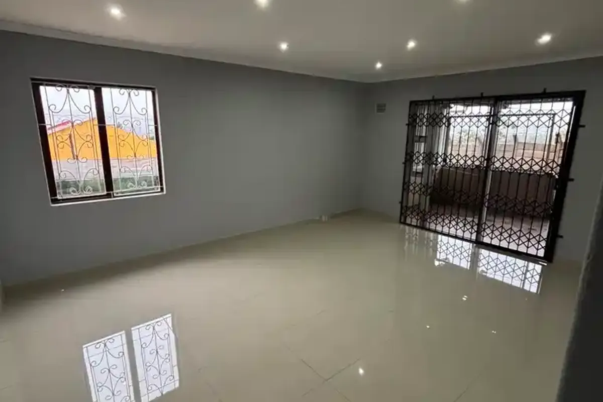 A spacious, empty living area featuring polished tiled flooring, recessed downlighting, and secure window and door fittings.