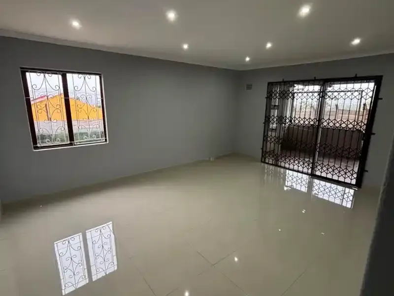 A spacious, empty living area featuring polished tiled flooring, recessed downlighting, and secure window and door fittings.
