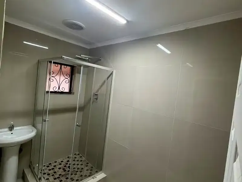 A clean, modern bathroom featuring a pedestal basin and a glass-enclosed shower with tiled finishes throughout.