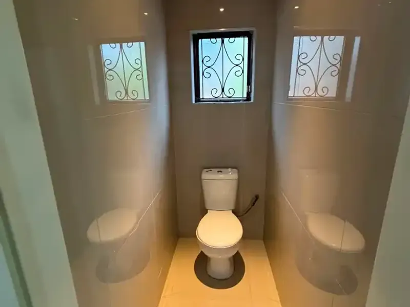 A compact, modern guest toilet featuring full-height wall tiling, polished floor tiles, and a secure window with decorative metal bars.