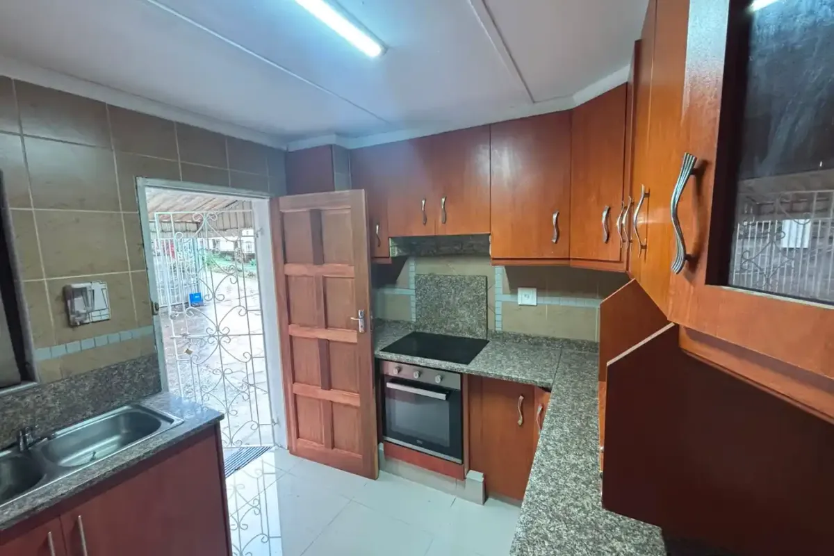 A functional kitchen featuring wooden cabinetry, granite countertops, a built-in oven and hob, and direct access to the exterior.