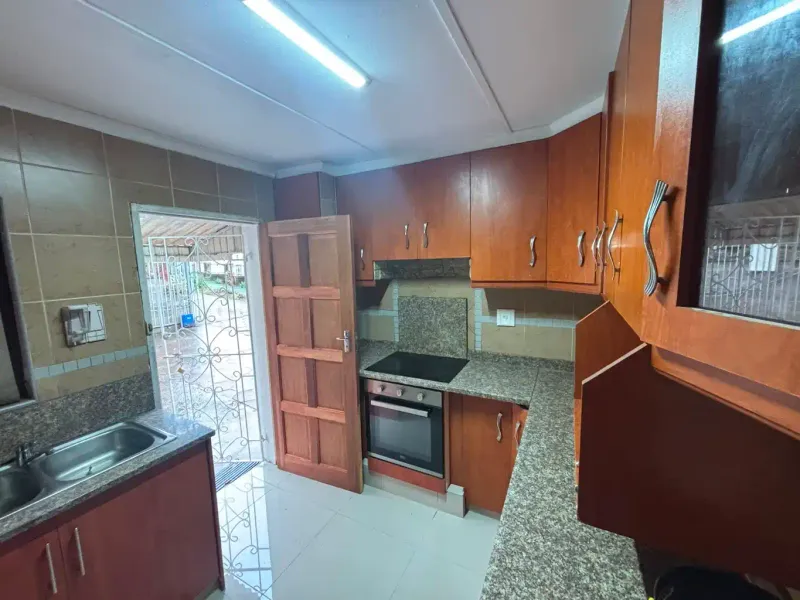 A functional kitchen featuring wooden cabinetry, granite countertops, a built-in oven and hob, and direct access to the exterior.