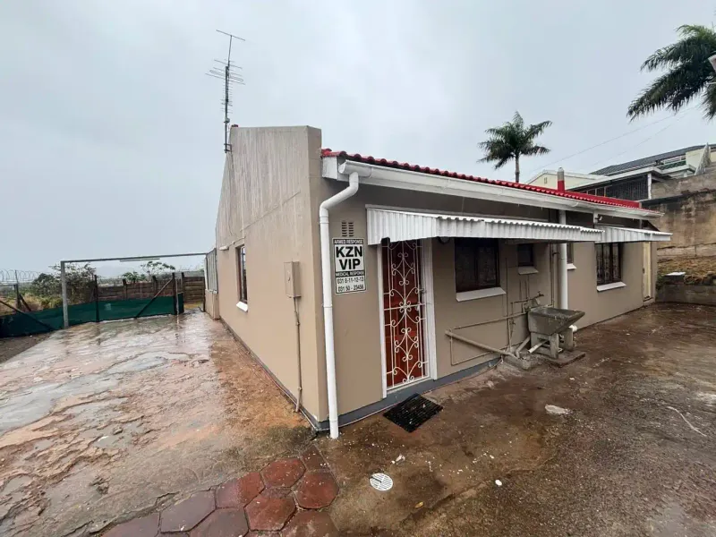 Rear exterior view of the property featuring a paved yard, external wash basin, security gate, and metal awnings.