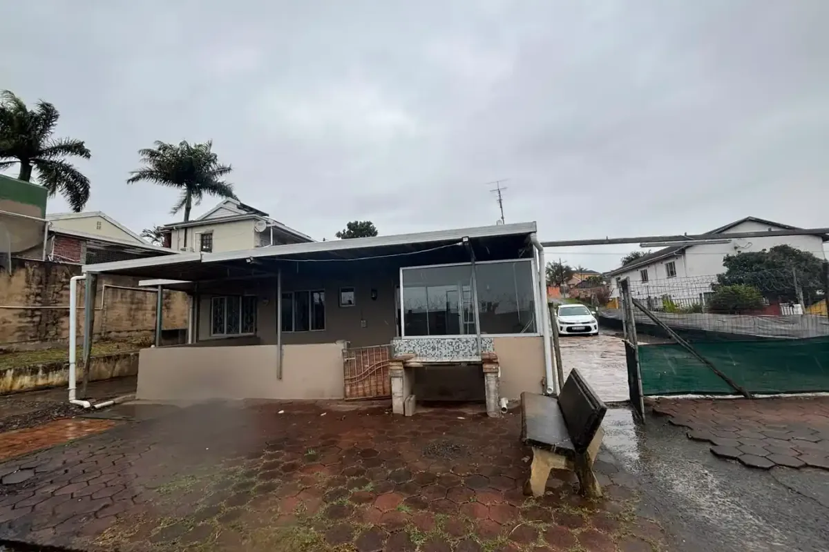 Rear exterior view of the property featuring a covered patio area, built-in braai, and paved outdoor space with perimeter fencing.