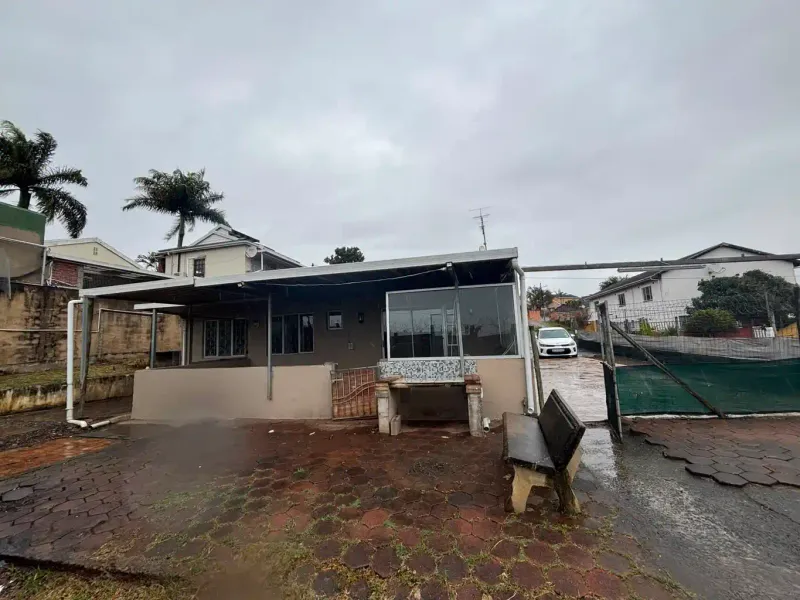 Rear exterior view of the property featuring a covered patio area, built-in braai, and paved outdoor space with perimeter fencing.