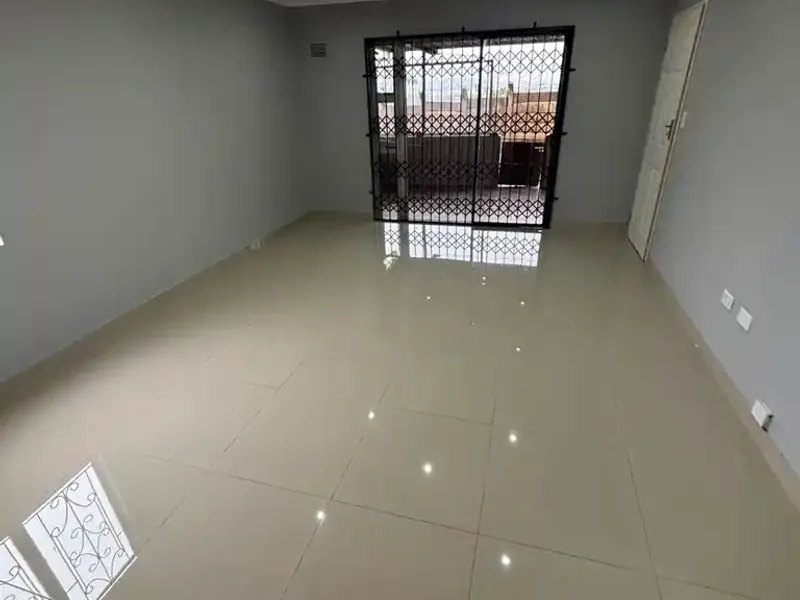 A spacious, empty living room featuring neutral grey walls, polished porcelain floor tiles, recessed downlighting, and a secure sliding glass door leading outdoors.