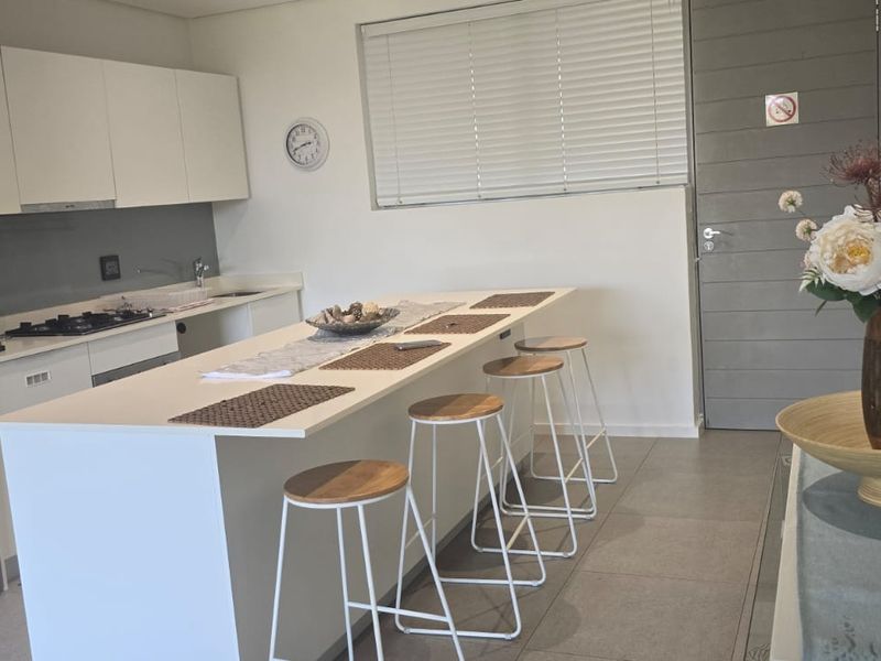 Modern kitchen featuring white cabinetry, a central island with breakfast bar seating, gas hob, and tiled flooring.