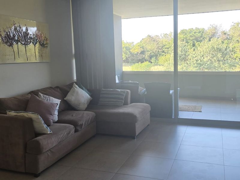 A bright living room featuring large sliding glass doors that open onto a balcony, providing natural light and views of the surrounding greenery.