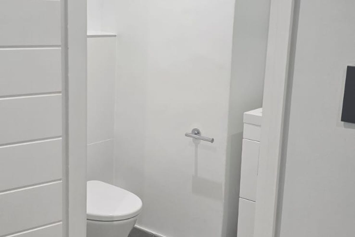 A clean, modern guest bathroom featuring a wall-hung toilet, vanity cabinet, and neutral grey floor tiling.