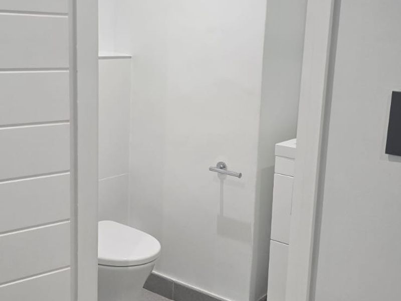 A clean, modern guest bathroom featuring a wall-hung toilet, vanity cabinet, and neutral grey floor tiling.
