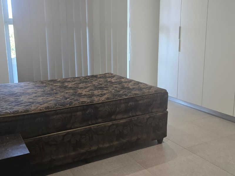 A bedroom featuring neutral tiled flooring, ample built-in cupboard storage, and vertical blinds allowing natural light.