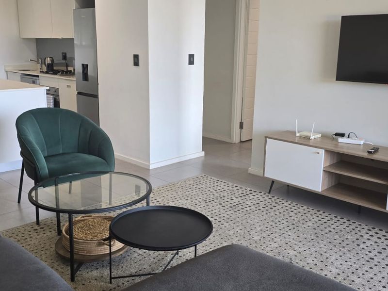 Modern open-plan living area featuring a kitchen with a central island and tiled flooring, seamlessly flowing into a comfortable lounge space.