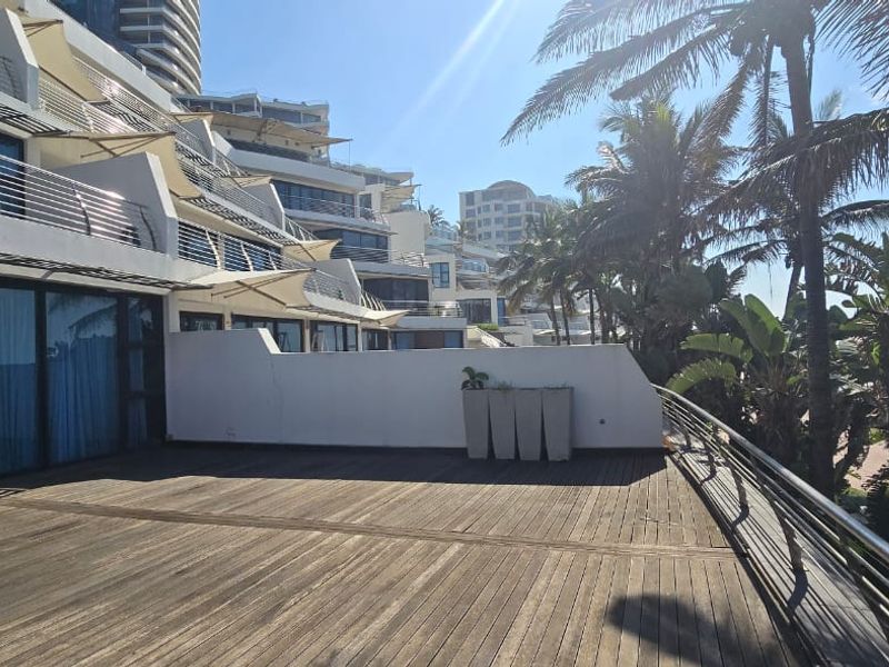 Spacious outdoor balcony featuring timber decking, stainless steel balustrades, and sliding glass doors, offering a bright and open terrace area.