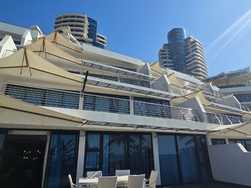 Rear elevation of a modern apartment complex featuring tiered balconies with stainless steel railings and tensioned shade sails.