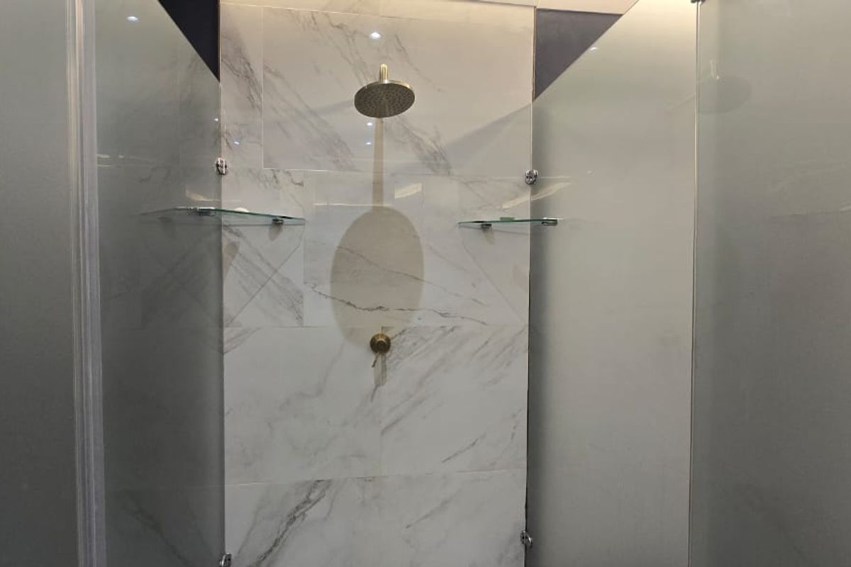 A modern walk-in shower featuring marble-look wall tiles, a rainfall shower head, and a sleek glass enclosure with integrated shelving.