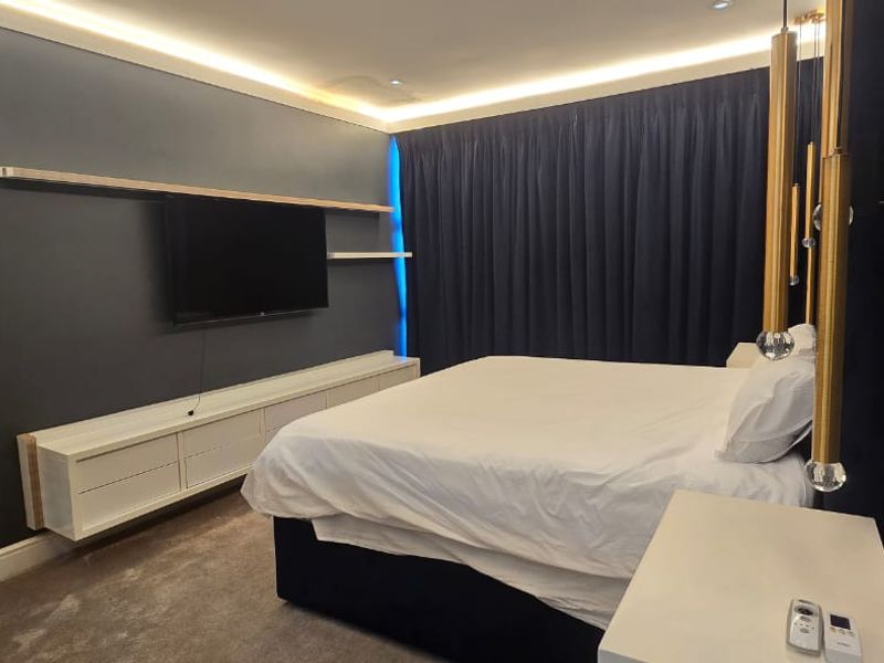 A modern, well-appointed bedroom featuring dark accent walls, built-in cabinetry, recessed ceiling lighting, and plush carpeting.