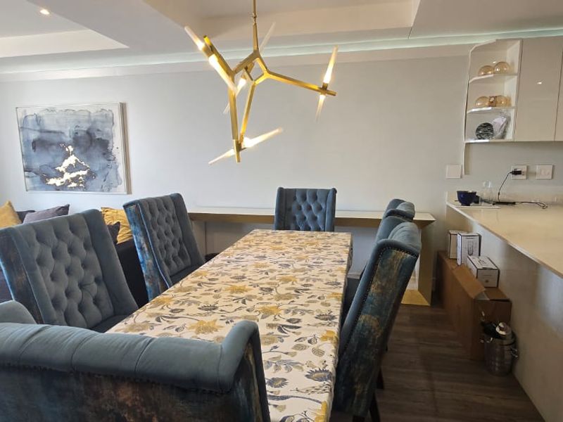 Modern open-plan living and dining area featuring high-gloss kitchen cabinetry, stone countertops, and recessed ceiling lighting, creating a cohesive and functional space.