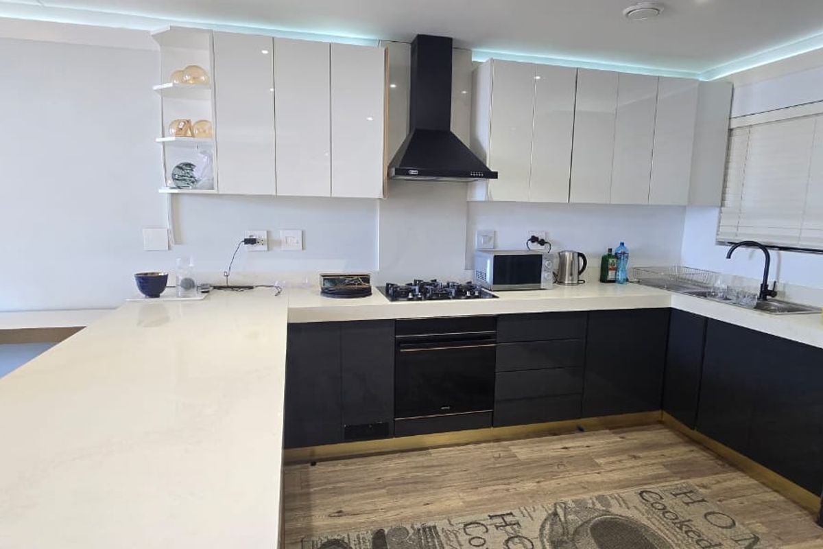 Modern kitchen featuring high-gloss cabinetry, stone countertops, integrated gas hob, electric oven, and a sleek extractor fan with recessed lighting.