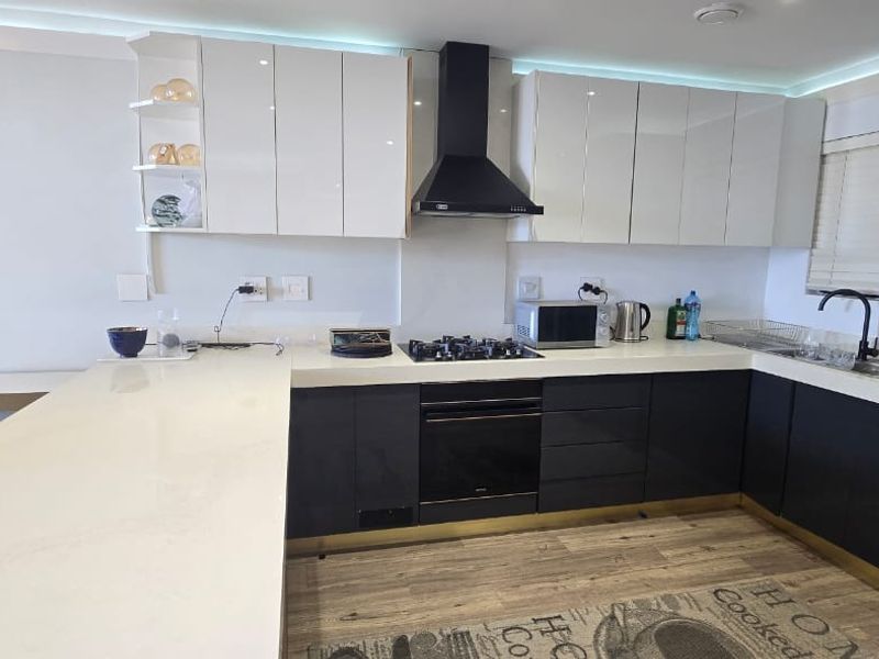 Modern kitchen featuring high-gloss cabinetry, stone countertops, integrated gas hob, electric oven, and a sleek extractor fan with recessed lighting.
