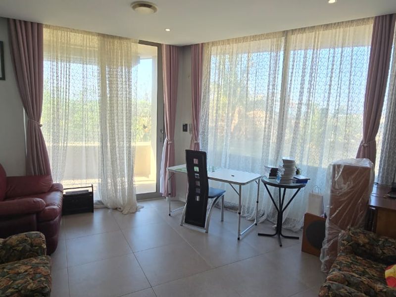 A bright living room featuring large sliding glass doors that open onto a balcony, complemented by neutral tiled flooring and recessed lighting.