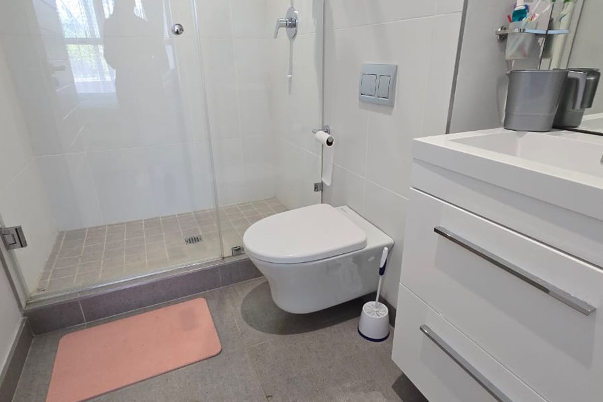 Modern bathroom featuring a wall-mounted toilet, glass shower enclosure, and a sleek white vanity cabinet with a basin.