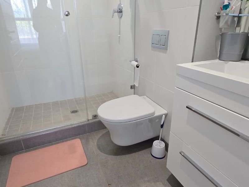 Modern bathroom featuring a wall-mounted toilet, glass shower enclosure, and a sleek white vanity cabinet with a basin.